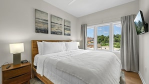 Ein Schlafzimmer mit Bett, Nachttisch, Lampe, Fernseher und einem Fenster mit Blick.