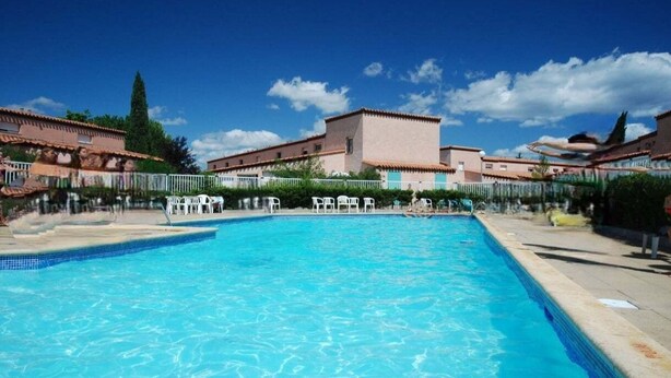 A swimming pool with clear blue water, surrounded by white lounge chairs and a building with a tiled roof. - Les jardins de Neptune, pool and relaxation (Saint-Cyprien)
