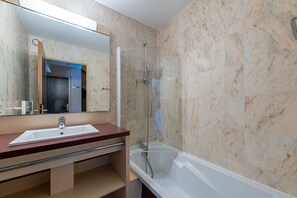 A bathroom with a marble wall, a sink, a mirror, and a shower.