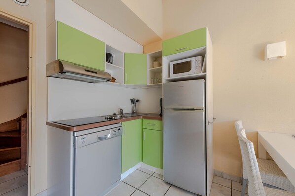 A compact kitchen with a dishwasher, microwave, and a small dining area with a chair.