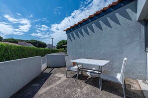 A patio with a table and chairs, a white wall, and a clear sky.