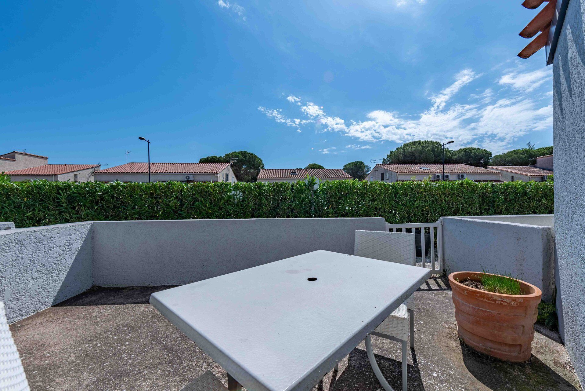 A rooftop terrace with a table and chairs, a potted plant, and a view of residential buildings.