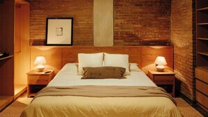 Hotellihuone, jossa on suuri sänky, kaksi yöpöytää valaisimineen, seinällä oleva kehystetty taulu ja tiiliseinä.