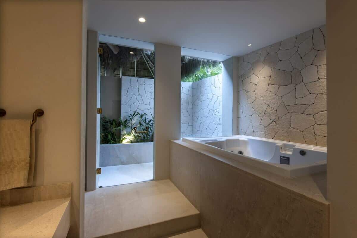 Une salle de bain moderne avec une grande baignoire, une porte en verre donnant sur un jardin et un mur en pierre.