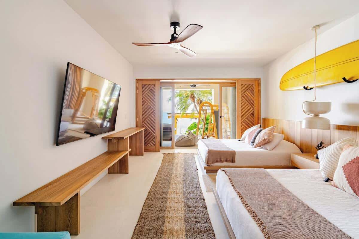 Una habitación de hotel moderna con una cama grande, un televisor, un ventilador de techo y una decoración con una tabla de surf.