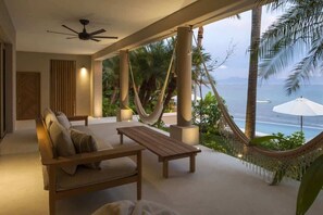 Ein moderner Außenbereich zum Sitzen mit einer Hängematte, einem Holztisch und Blick auf das Meer.