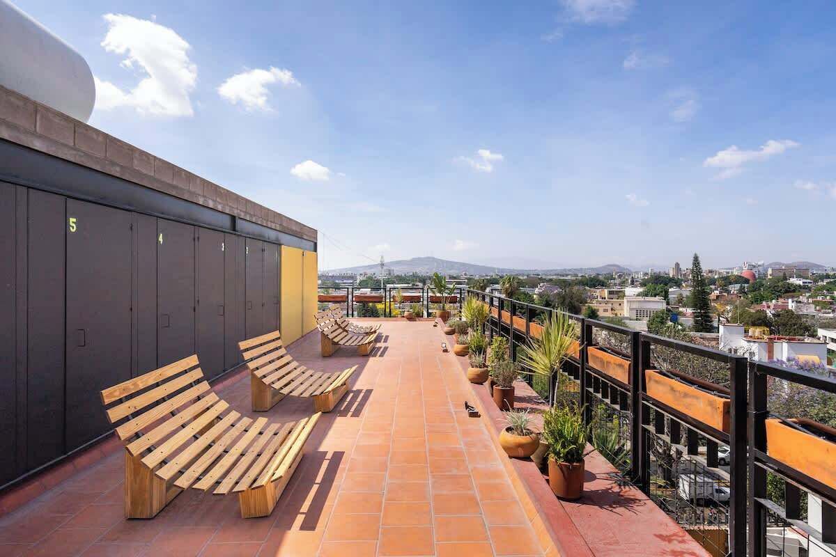 Terraço no telhado com bancos, plantas em vasos e vista para a cidade.