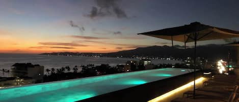 Une piscine avec vue sur l’océan et les montagnes, au crépuscule.