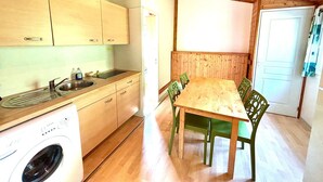 A compact kitchen with wooden cabinets, a built-in washing machine, and a dining area with a wooden table and chairs. - Les noisetiers du Neyrial, quiet and countryside (Yssingeaux)