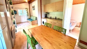 A compact kitchen with wooden cabinets, a dining table with chairs, a built-in bench with cushions, and a washing machine. - Les noisetiers du Neyrial, quiet and countryside (Yssingeaux)