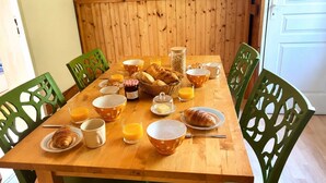 A wooden dining table with breakfast items, green chairs, and a wooden wall. - Les noisetiers du Neyrial, quiet and countryside (Yssingeaux)