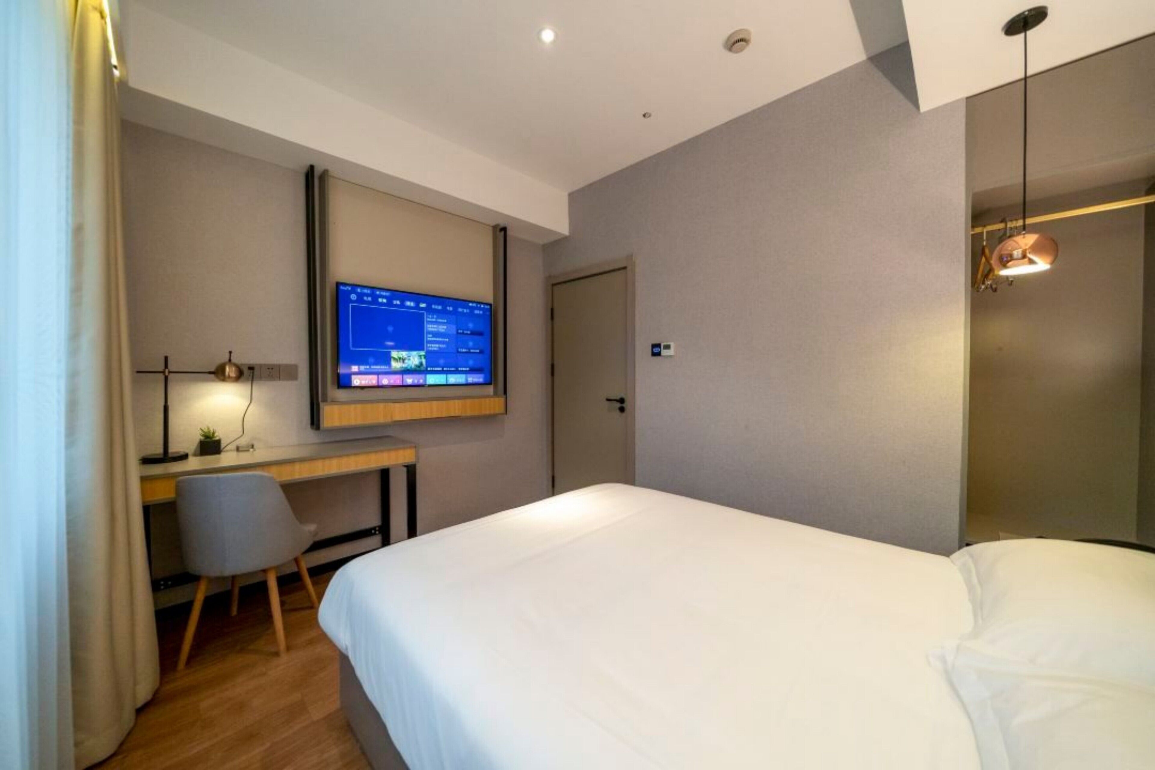 Habitación de hotel con cama, escritorio, monitor de computadora, silla y puerta.