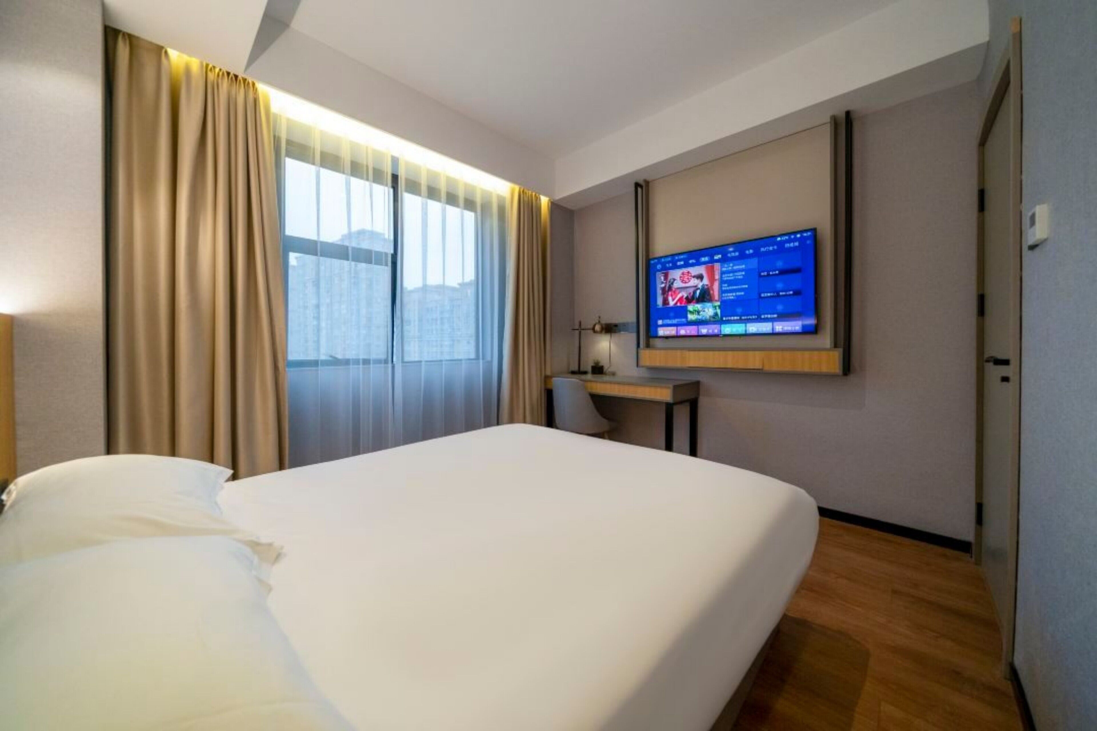 Habitación de hotel con cama, escritorio, televisor y ventana con cortinas.