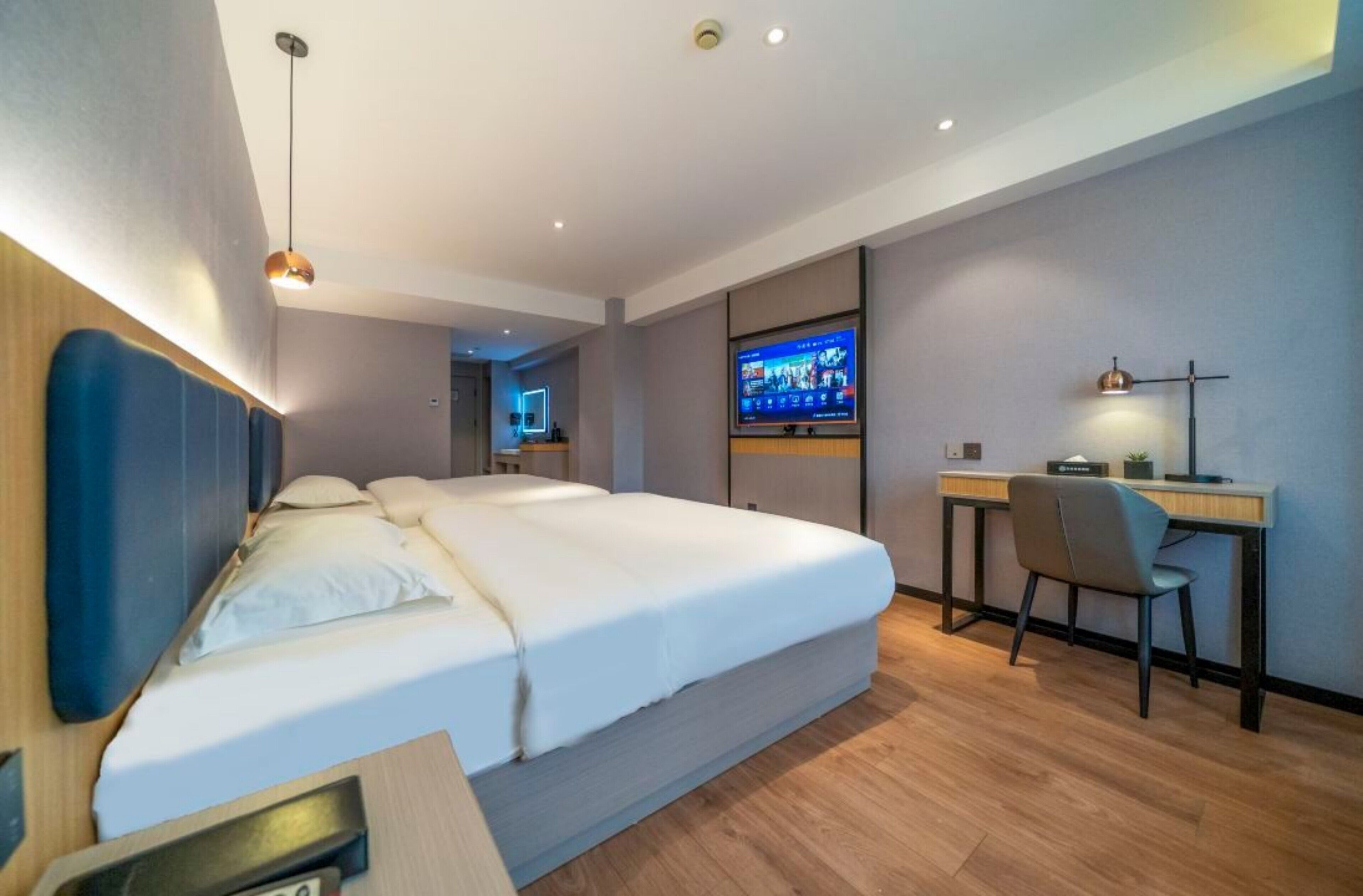 Een moderne hotelkamer met een groot bed, een bureau met stoel, een televisie en een kleine bureaulamp.