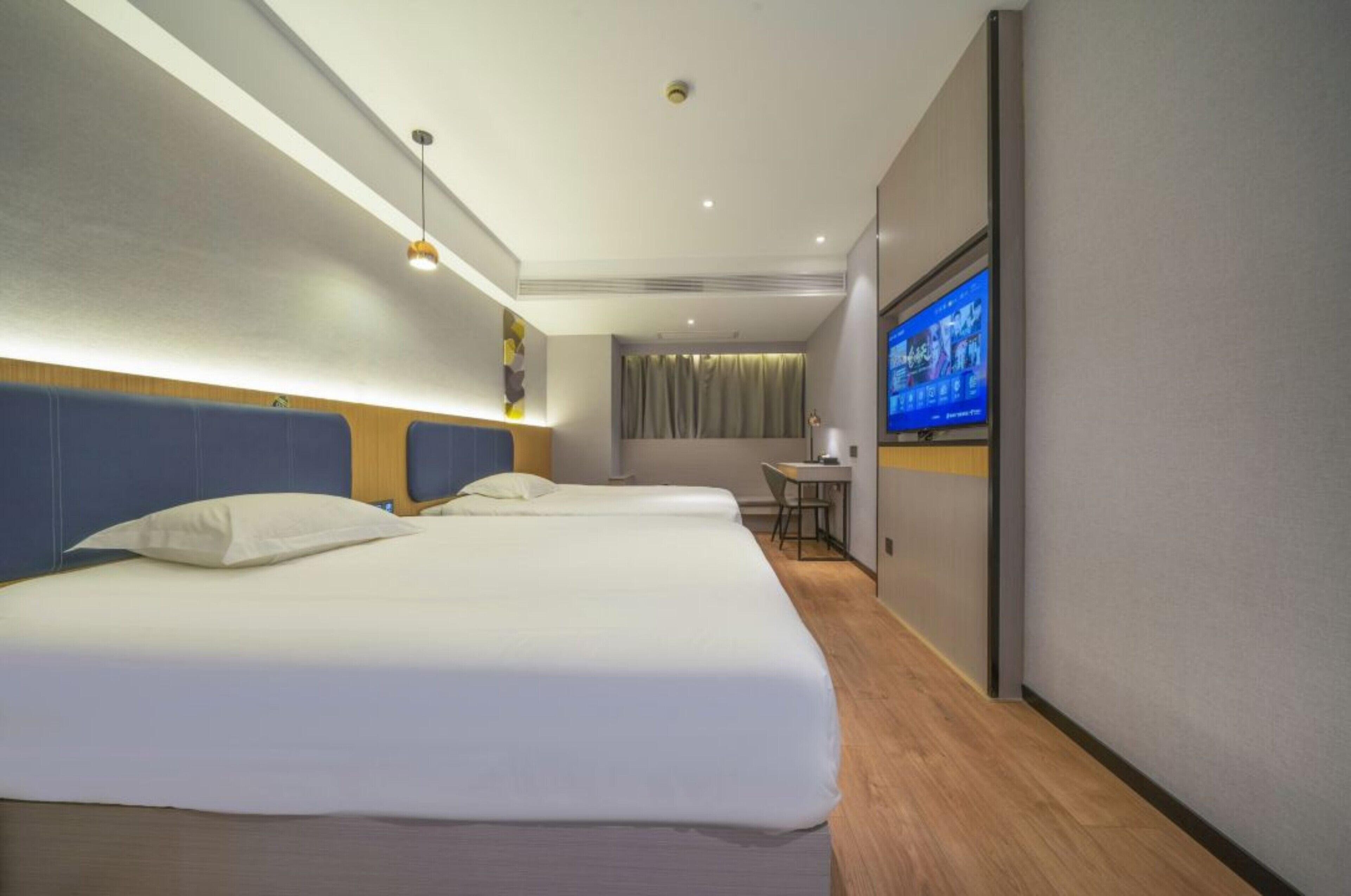 A hotel room with two beds, a desk, a television, and a curtain.