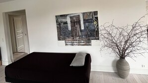 Une pièce avec un canapé noir, un grand tableau abstrait, une plante en pot et un plancher en bois.