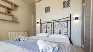 Een net opgemaakt bed met opgerolde handdoeken, een radiator en wandlampen.