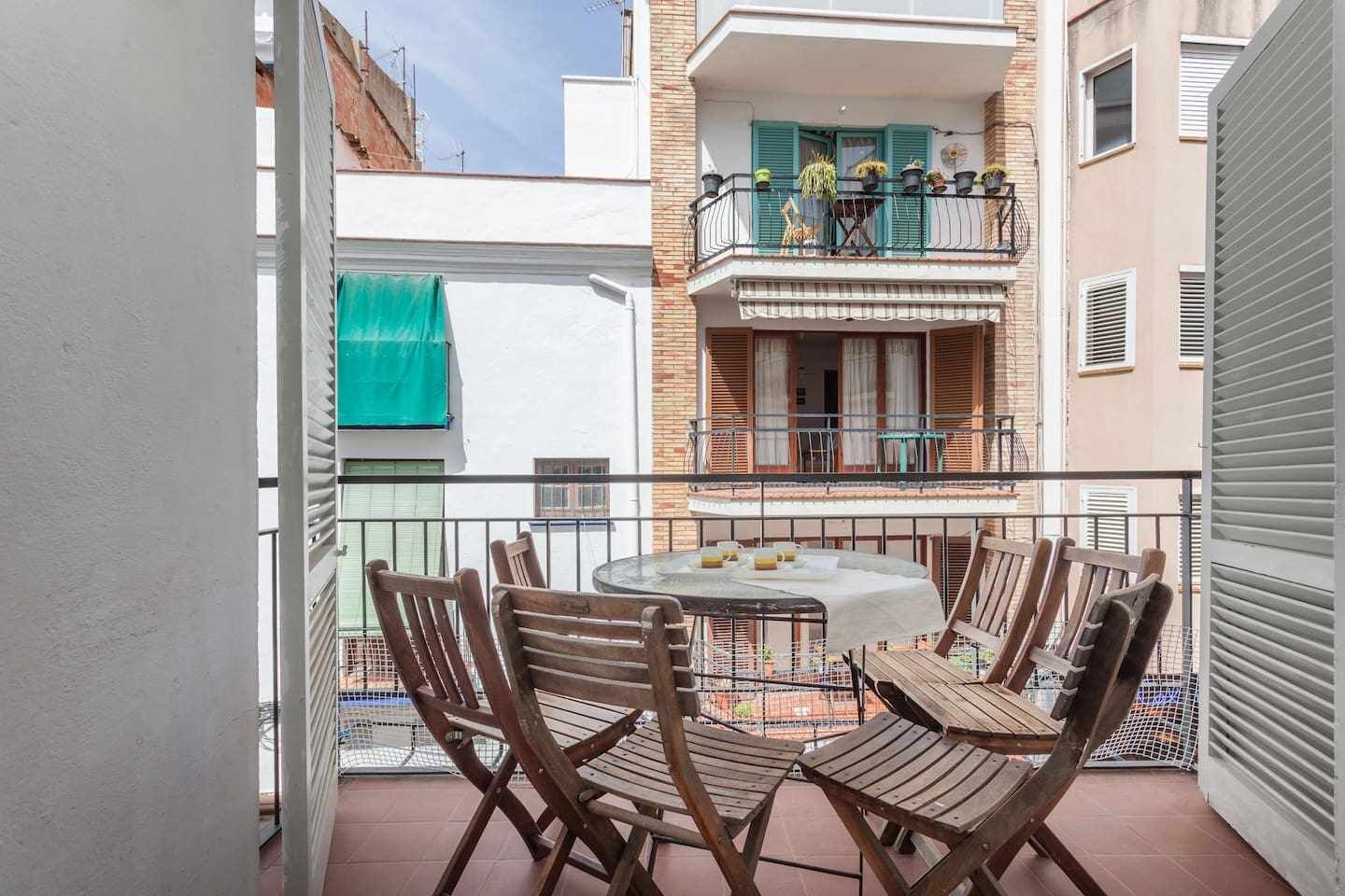A balcony with a round table and wooden chairs, a view of a neighboring building, and a green awning.