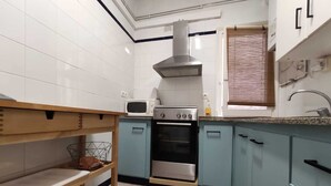 Een keuken met witte betegelde wanden, een roestvrijstalen afzuigkap, een magnetron, een oven en lichtblauwe kastjes.
