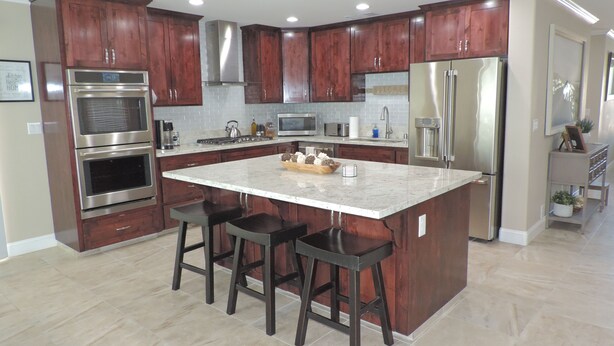 Una cocina moderna con armarios de madera oscura, electrodomésticos de acero inoxidable, una isla central con taburetes de bar y suelo de baldosas.