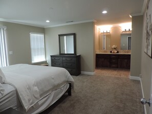 A bedroom with a bed, dresser, mirror, and a bathroom with a sink and vanity. - Clovis Foothill Retreat, Spa, BBQ & Mountain Views (Clovis)