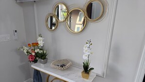 Une console en marbre blanc agrémentée de détails dorés, un vase rempli d’orchidées blanches et un ensemble de miroirs décoratifs disposés sur le mur.