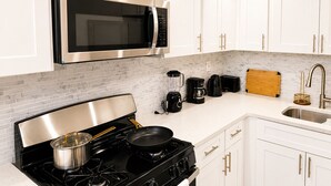 Une cuisine moderne avec des meubles blancs, un four à micro-ondes en acier inoxydable, une cuisinière à gaz, une machine à café et un évier.