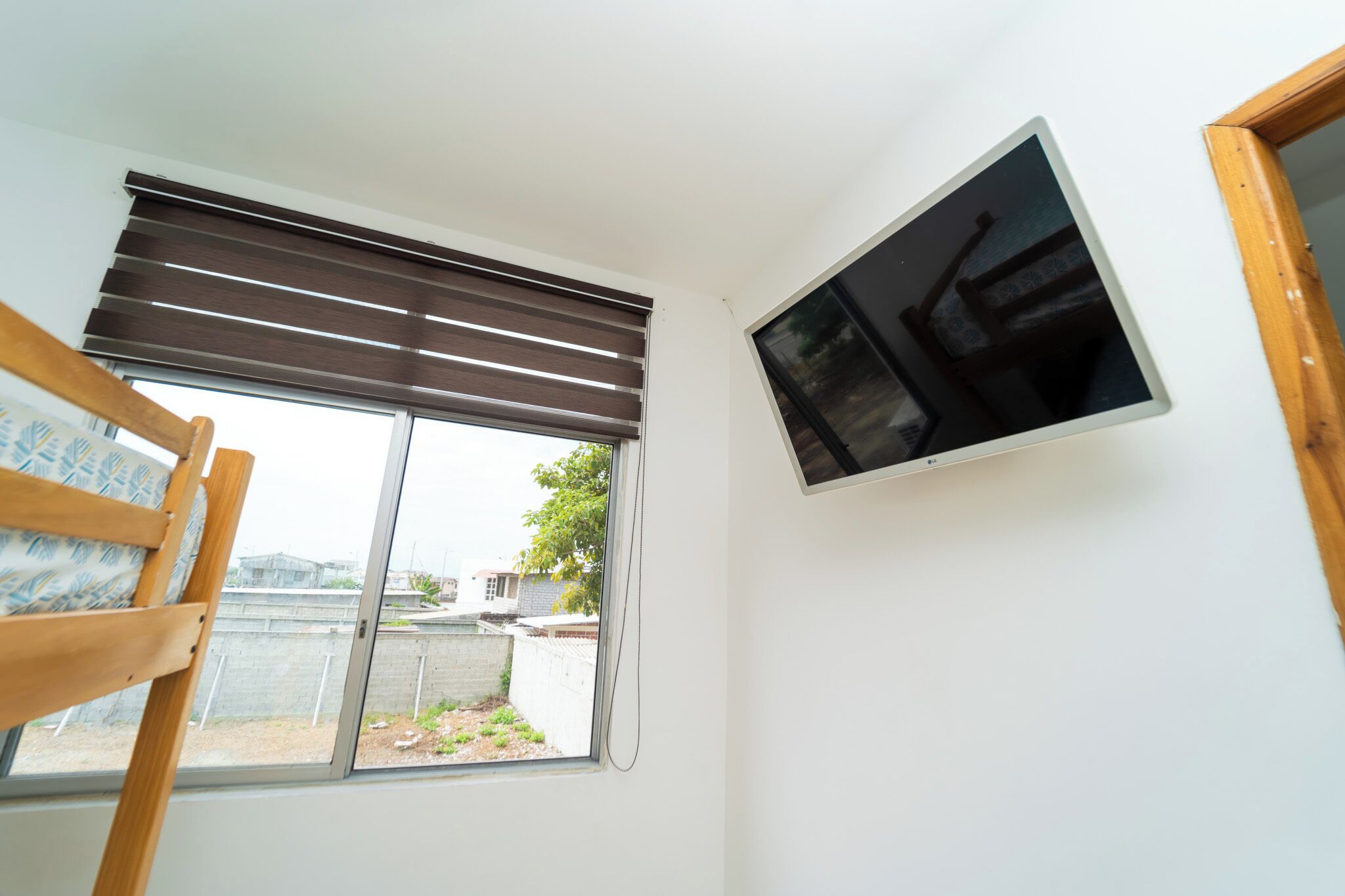 Una habitación con ventana, televisor montado en la pared y una cama de madera.