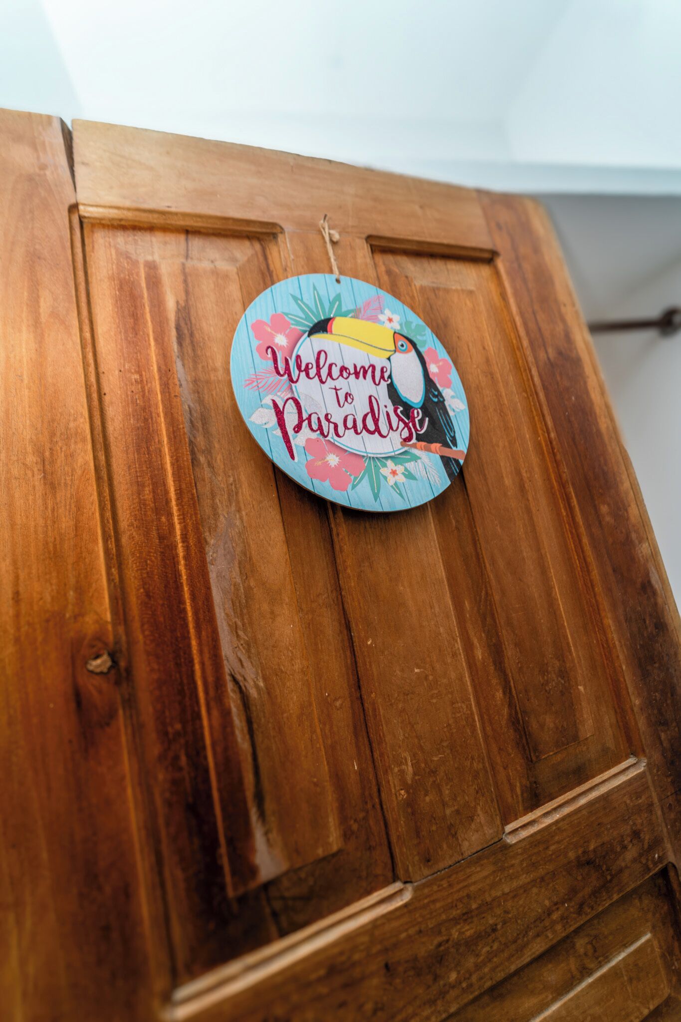 Una porta in legno con un cartello circolare che riporta la scritta 'Welcome to Paradise'.