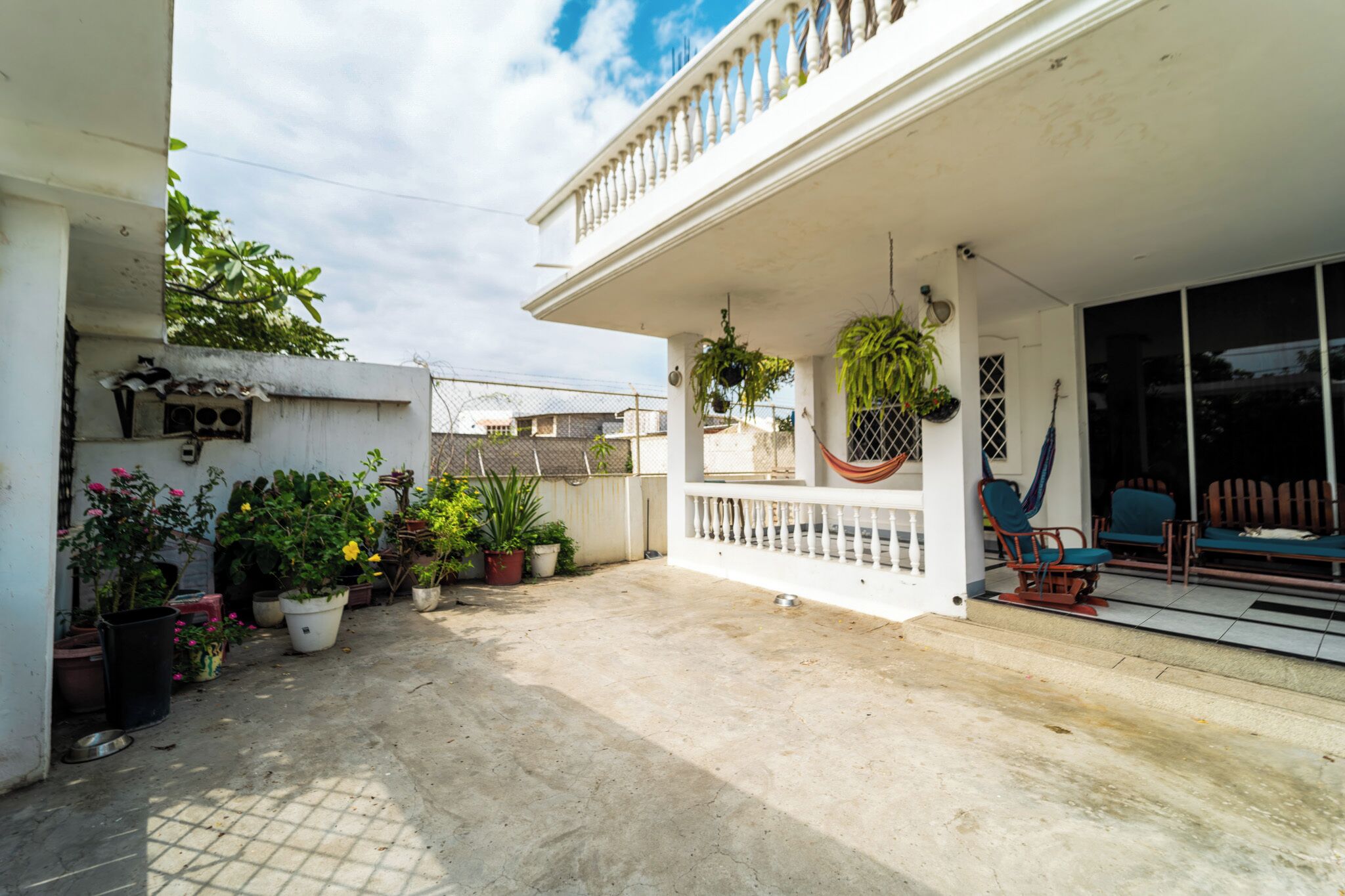 A covered patio area with potted plants, outdoor furniture, and a white railing.