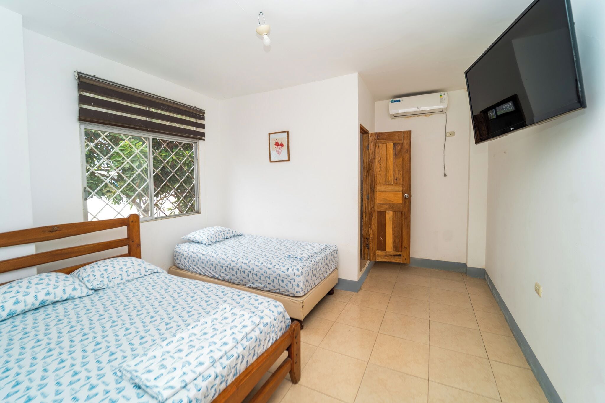 A bedroom with two beds, a TV, and a window with blinds.