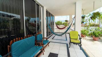 A balcony with a hammock, chairs, and potted plants.