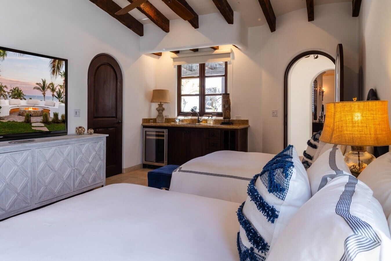 A hotel room with two beds, a TV, a desk with a lamp, and a window.