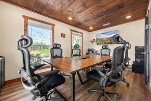 Un salón de conferencias con una mesa de madera, cuatro sillas de oficina negras, un cuadro en la pared y una ventana con vistas a zonas verdes.