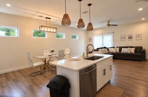 A modern kitchen with a central island, white cabinetry, and a dining area with a glass table. - Modern 3BR Retreat l Sleeps 7 l 7 Parking Spaces Southeast Houston (Houston)