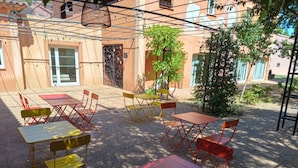 An outdoor seating area with tables and chairs, a decorative metal gate, and a building with a tiled roof in the background. - Le Clos du Thoronet (Le Thoronet)