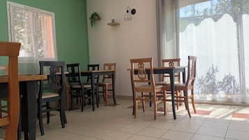 Un espace repas avec des tables et des chaises en bois, un mur végétal, une fenêtre ornée de rideaux légers et une vue sur les arbres à l’extérieur.