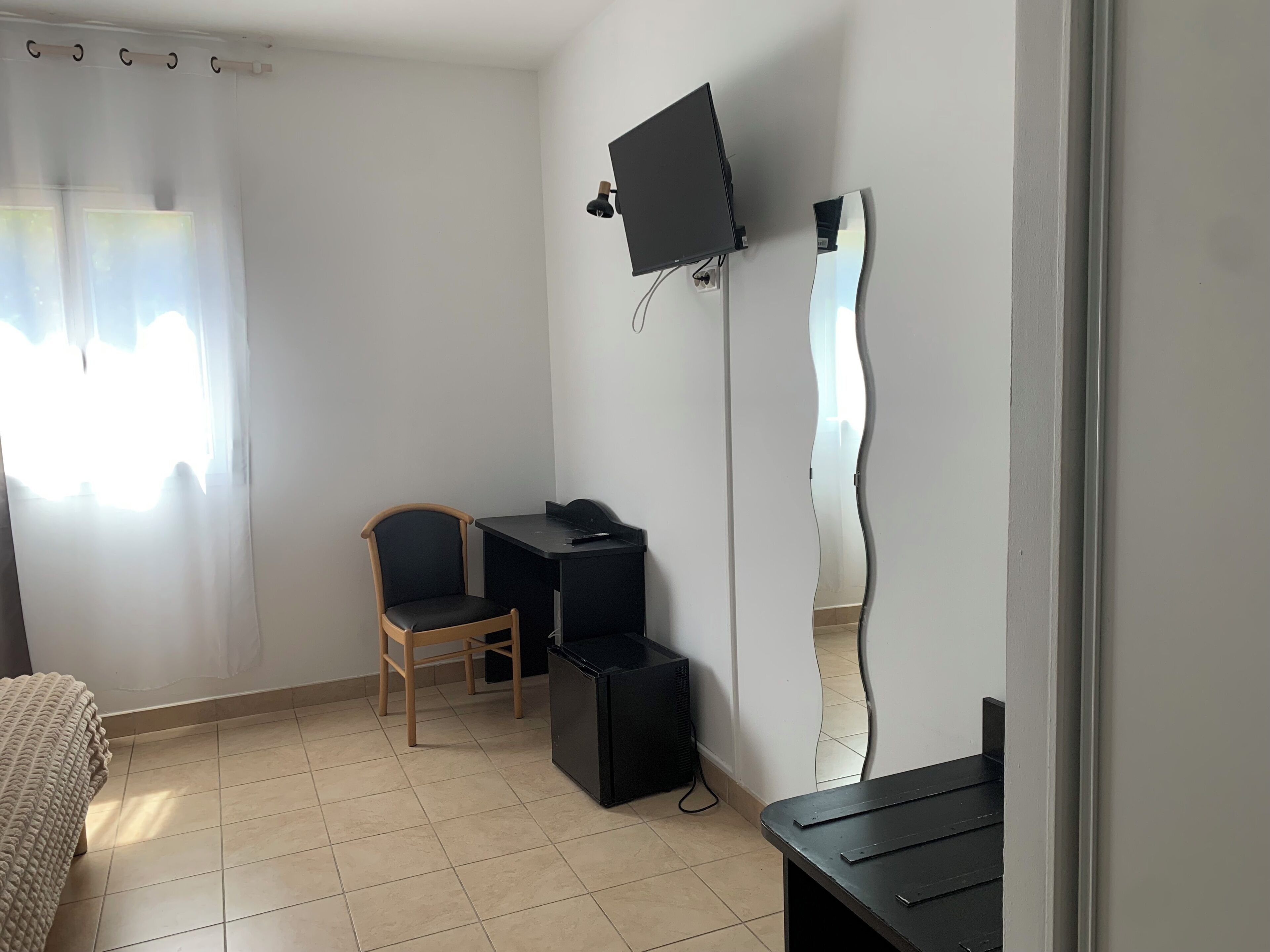 A room with a desk, chair, television, and a large mirror.