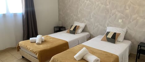 Hotelkamer met twee bedden, elk met een bruine sprei en witte lakens, een gestructureerde muur en een klein nachtkastje met een lamp.