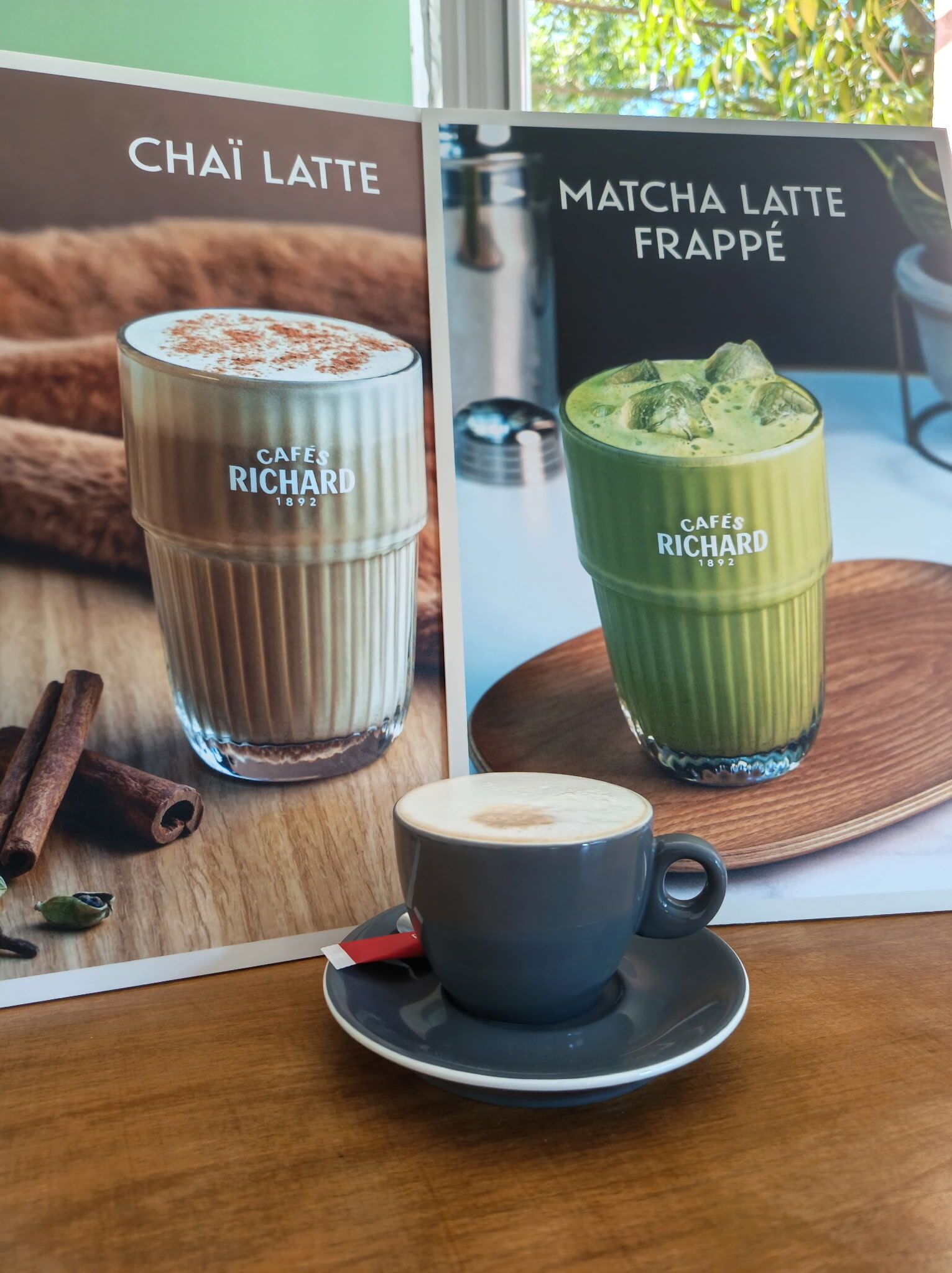Un panneau affichant le menu avec deux options de boissons, une tasse de café et une table en bois.
