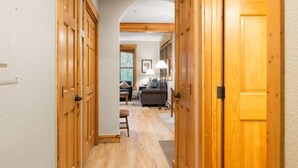 Un couloir avec des portes en bois qui donnent sur un salon équipé d’un canapé et d’une lampe.