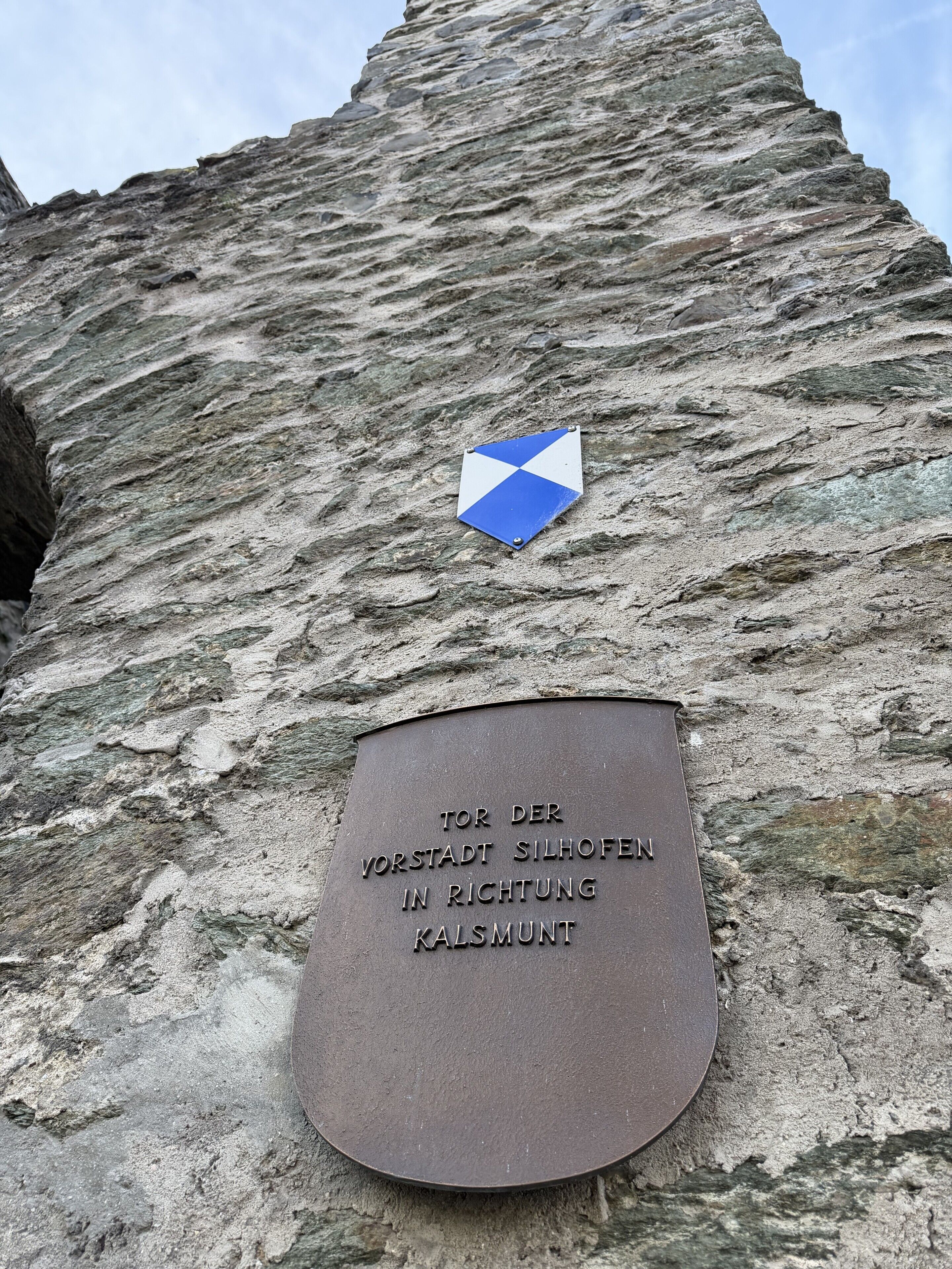 Eine Steinsäule mit einer Gedenktafel und einem blau-weißen Schild.
