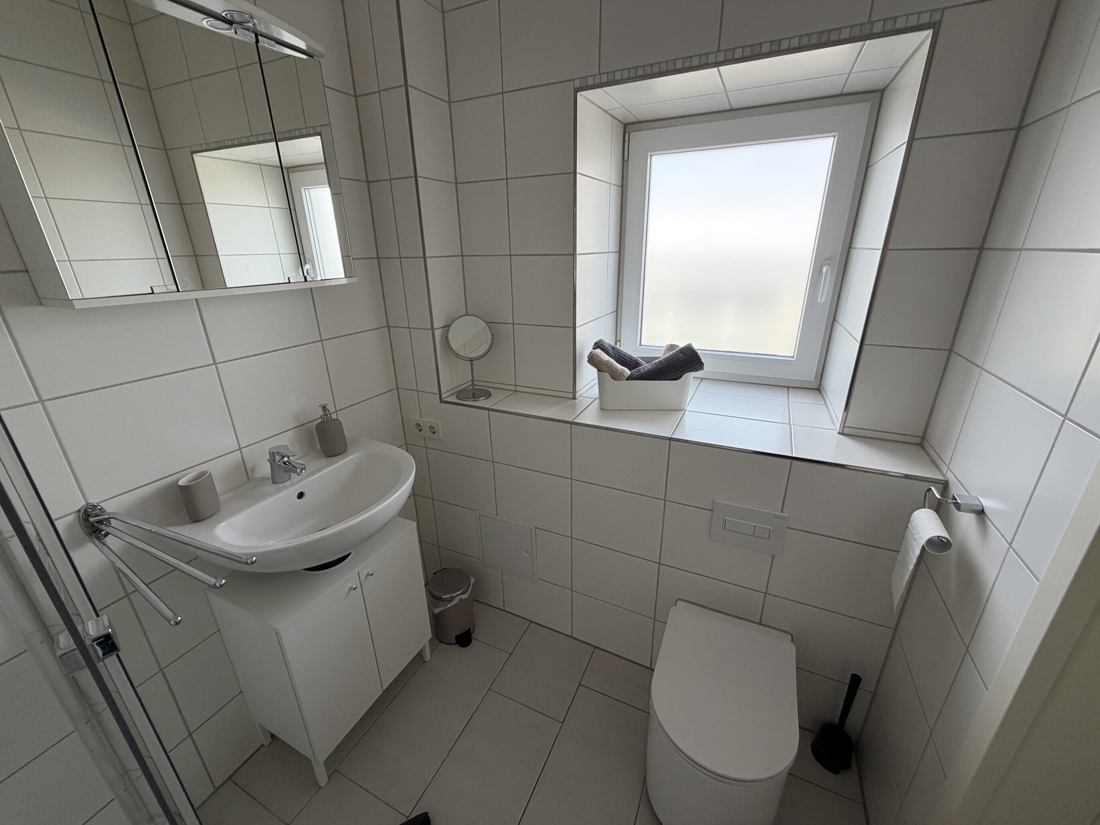 Un baño moderno con lavamanos, espejo, inodoro y ventana.