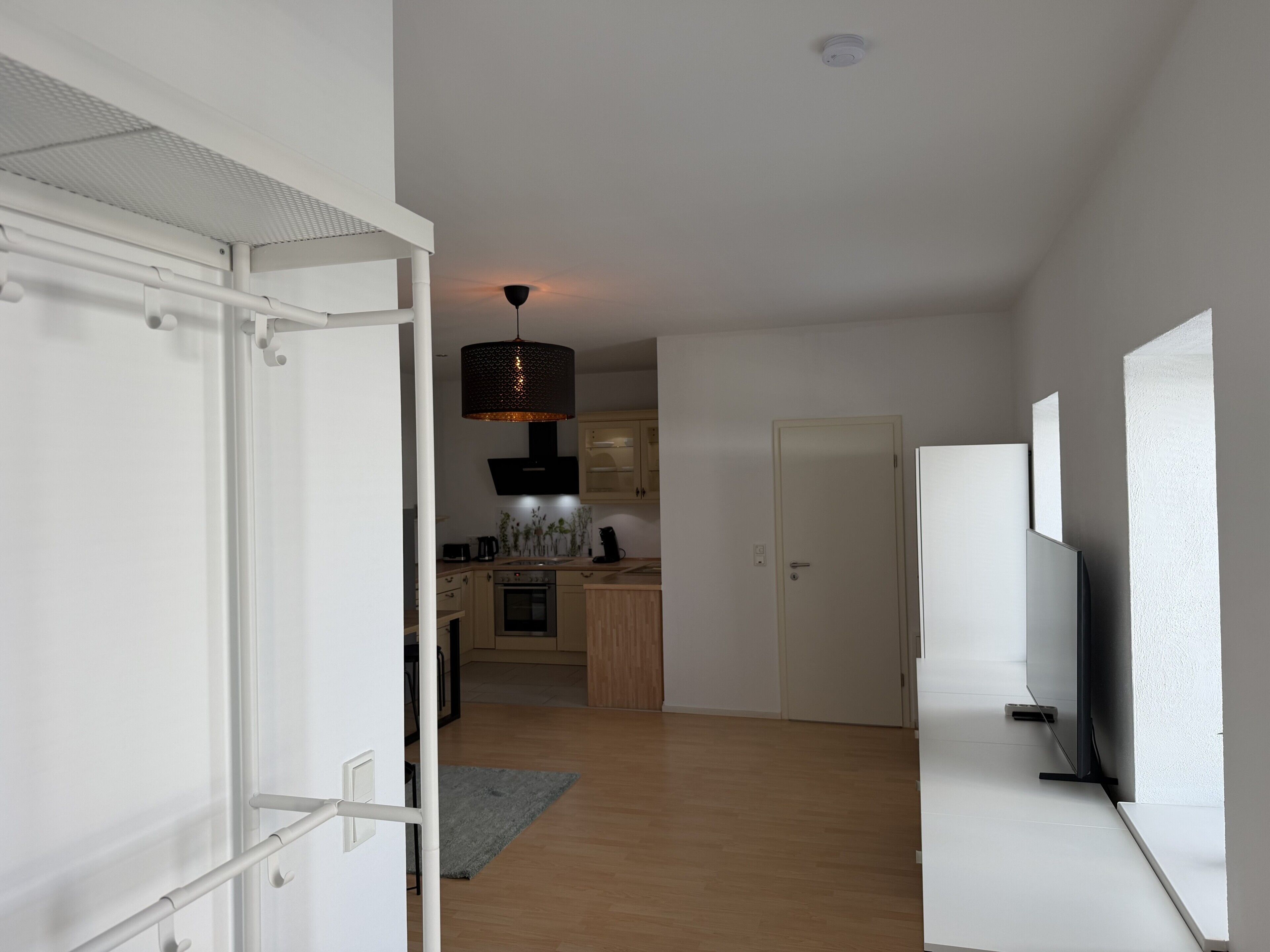 Una cocina moderna con una isla central, un comedor con mesa y sillas, y un pasillo que lleva a una puerta.