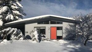 Ein modernes, zweistöckiges Gebäude mit schneebedecktem Dach und roter Tür.