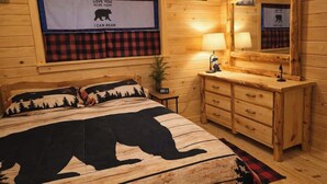 A wooden cabin bedroom with a bed featuring a bear design, a dresser, a mirror, and a window with a bear poster. - Rustic Tiny Cabin retreat with AC (Union Mills)