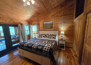 A wooden cabin bedroom with a bed, two bedside lamps, a nightstand, and a window with curtains. - Hideaway Hollow Cabin, Mtn view, Bed swing, hot tub near Ocoee River/Copperhi... (Murphy)