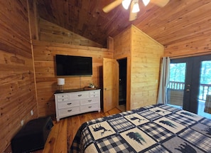 A wooden cabin bedroom with a bed, dresser, TV, and a door leading to a balcony. - Hideaway Hollow Cabin, Mtn view, Bed swing, hot tub near Ocoee River/Copperhi... (Murphy)