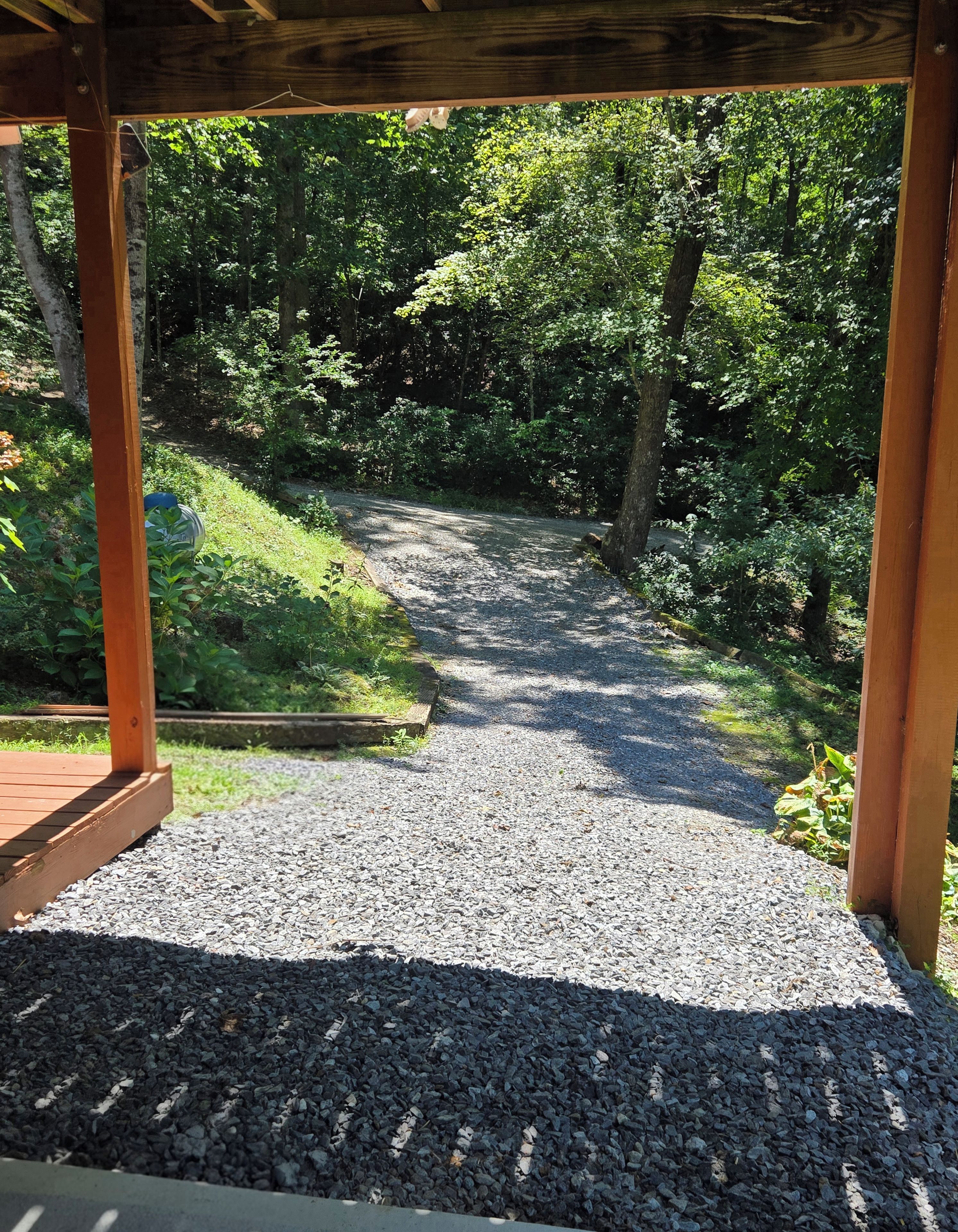 Un sentier de gravier mène à une zone boisée, bordée de structures en bois.