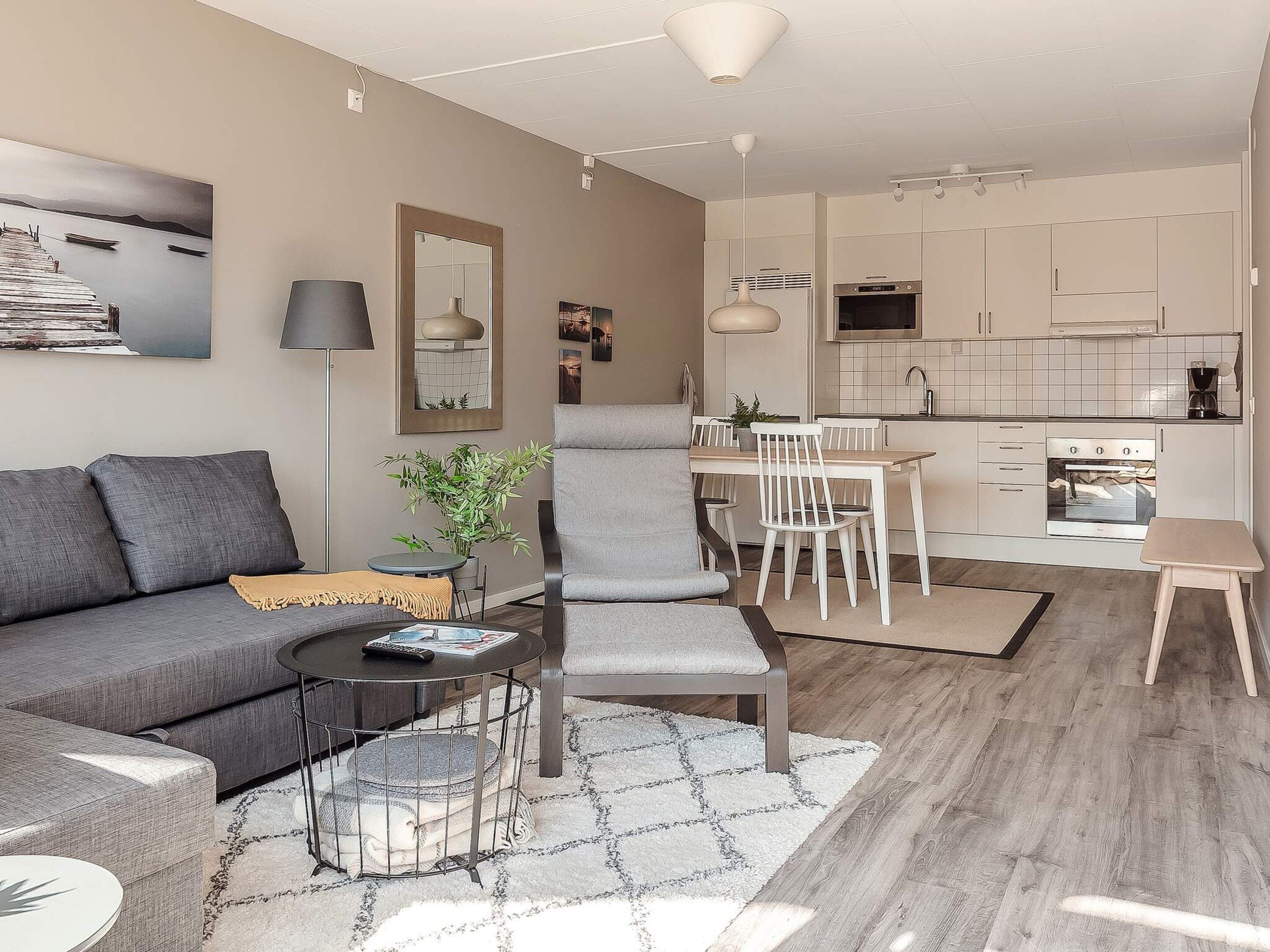 A modern living room with a grey sofa, a coffee table, and a dining area with a white table and chairs.